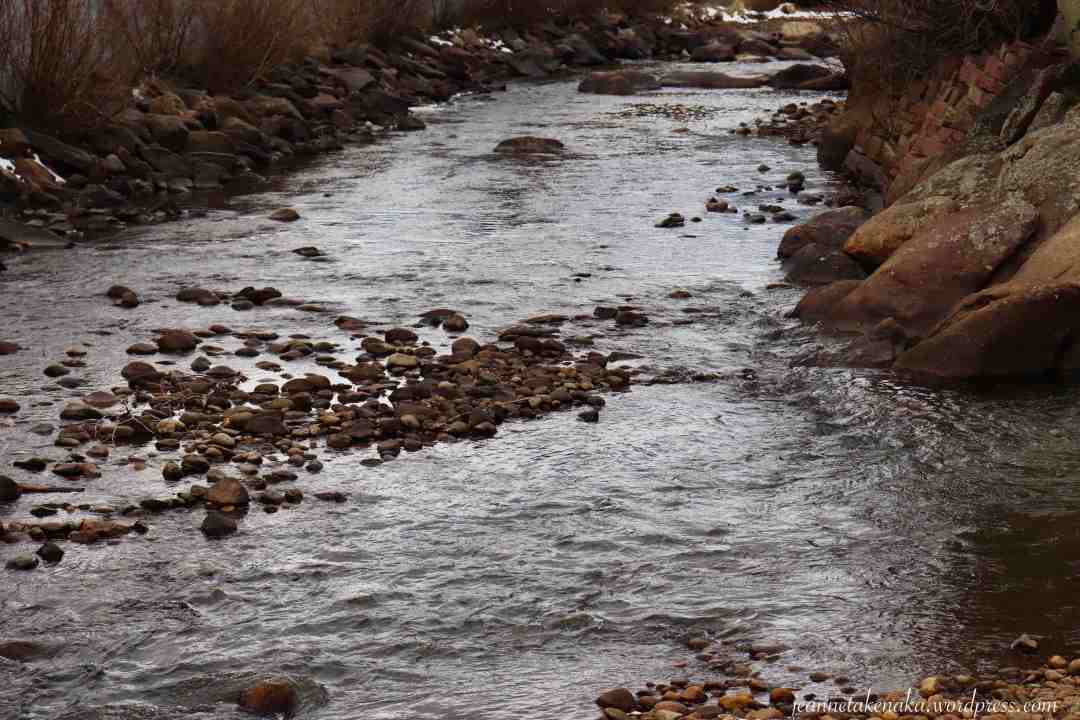 A calm river running around smaller rocks with larger rocks bordering each side of the water